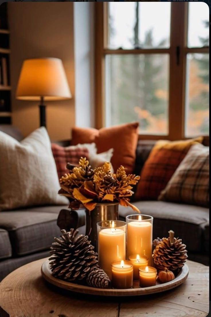 candles and pine cones on a tray in front of a couch