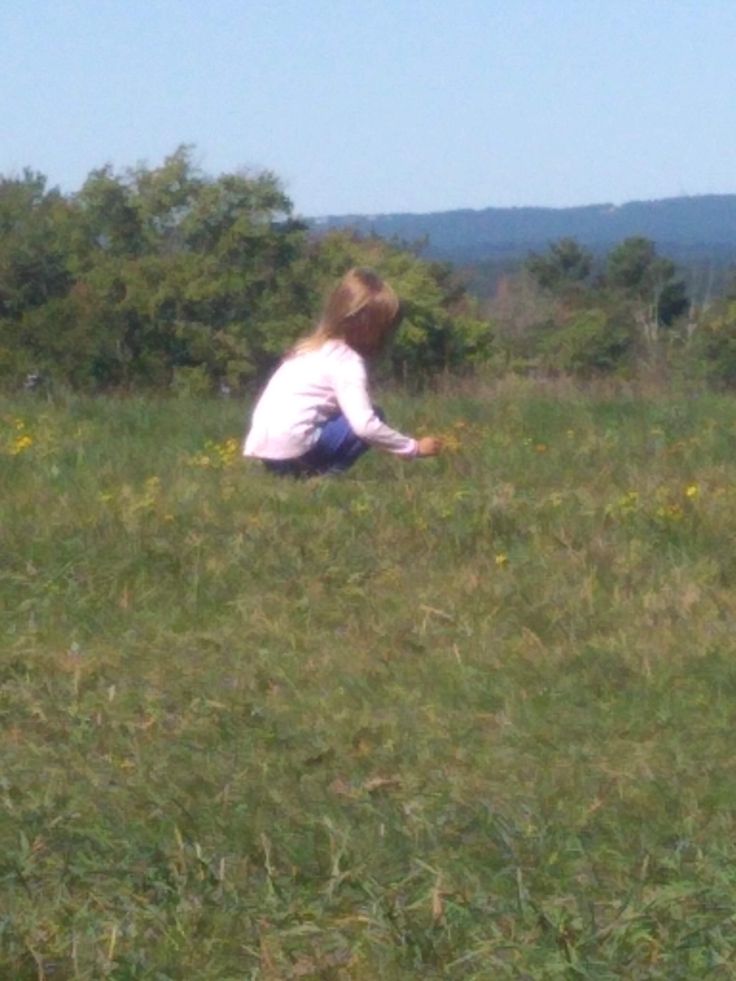 a woman kneeling down in the grass with a frisbee on her hand and trees in the background