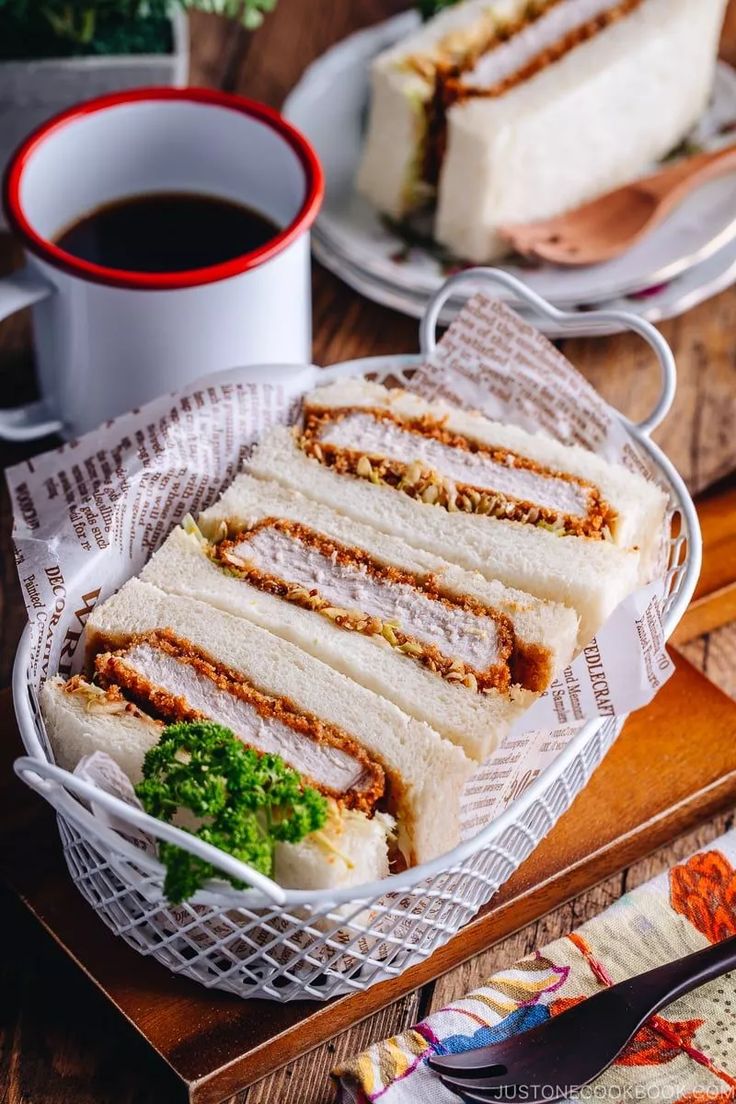 two plates with sandwiches on them next to a cup of coffee and spoons in the background