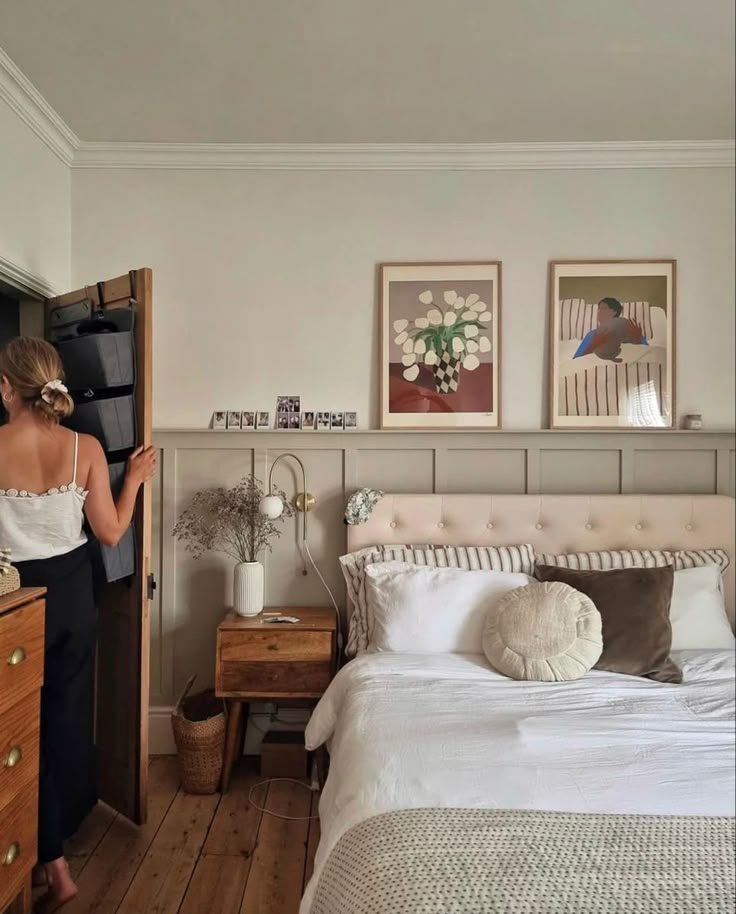 a woman standing next to a bed in a room with white walls and wooden floors