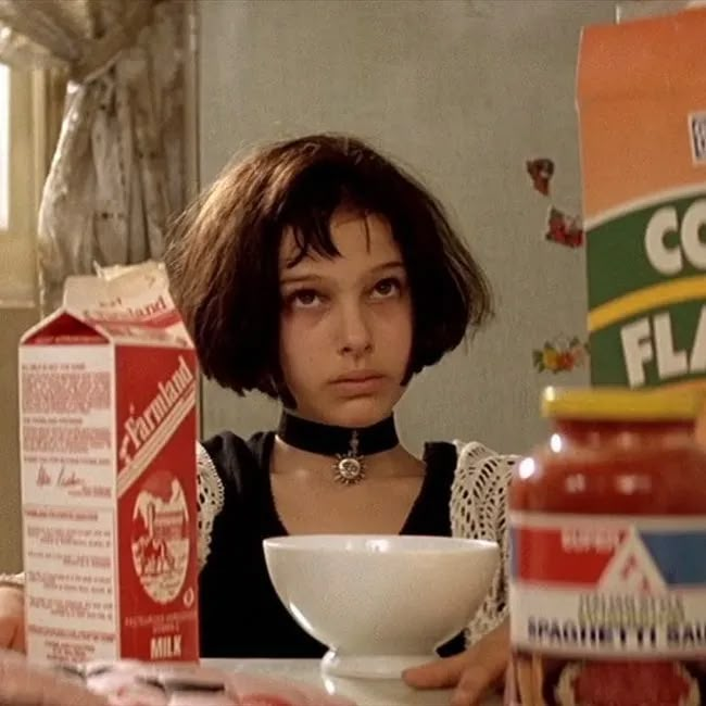 a woman sitting at a table with some food in front of her and a carton of cornflakes behind her