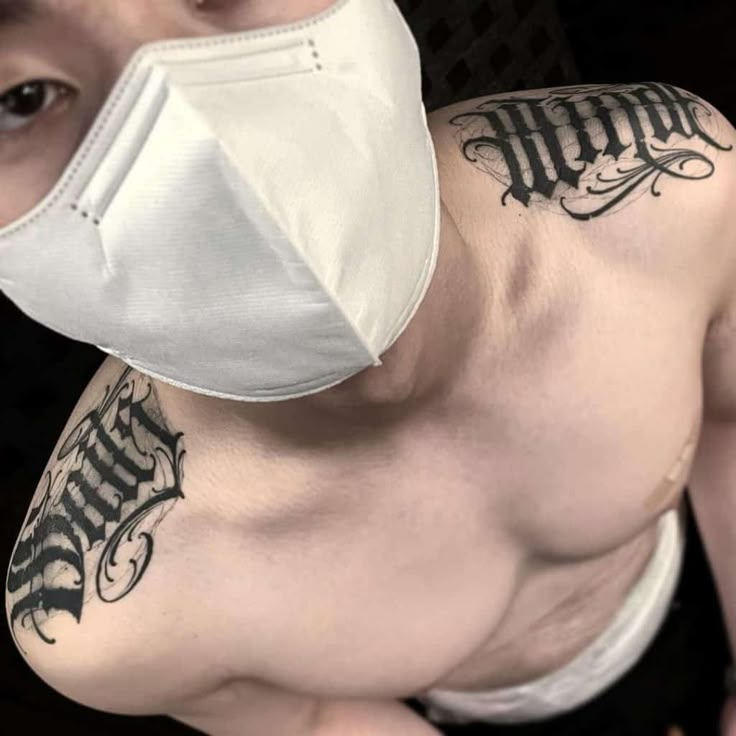 a shirtless man wearing a face mask with tattoos on his chest and shoulder, looking at the camera