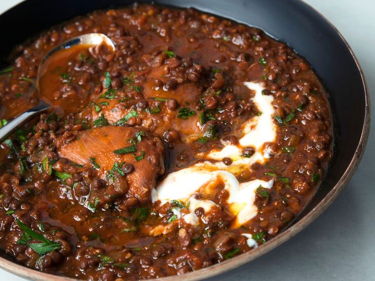 a bowl filled with meat and sauce on top of a white tablecloth next to a spoon