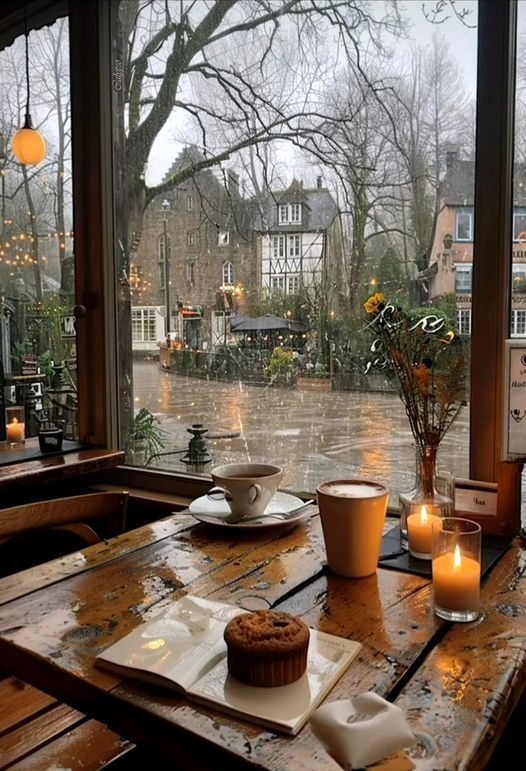 a wooden table topped with a cupcake next to a window covered in raindrops