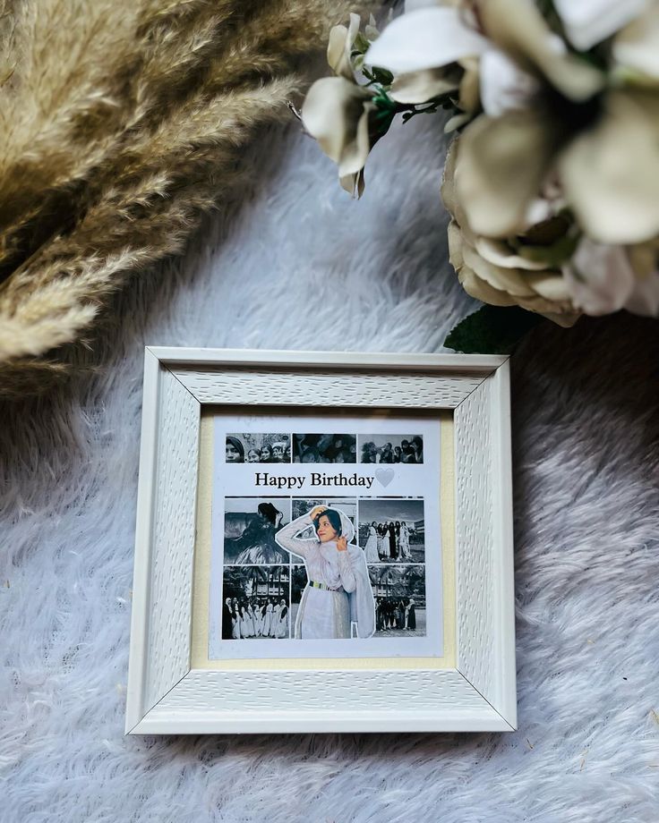 a white frame with a happy birthday photo on it next to some flowers and fur