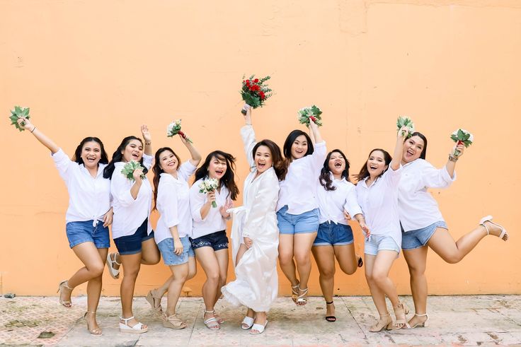 a group of women standing next to each other in front of a wall holding flowers