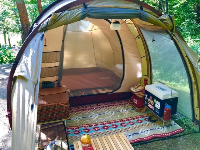 a tent is set up in the woods with picnic tables and coolers on it