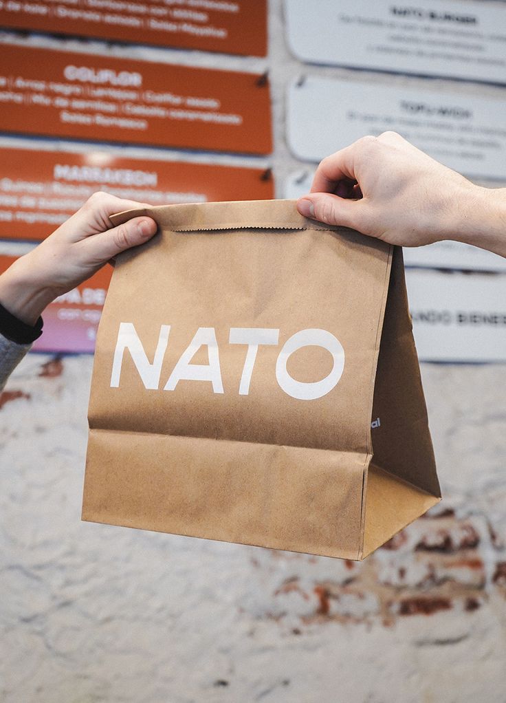 two hands holding a brown paper bag with the word natto on it in white lettering