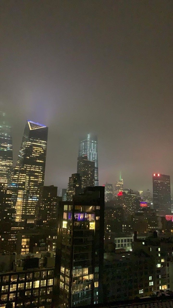 the city skyline is lit up at night with skyscrapers in the foggy sky