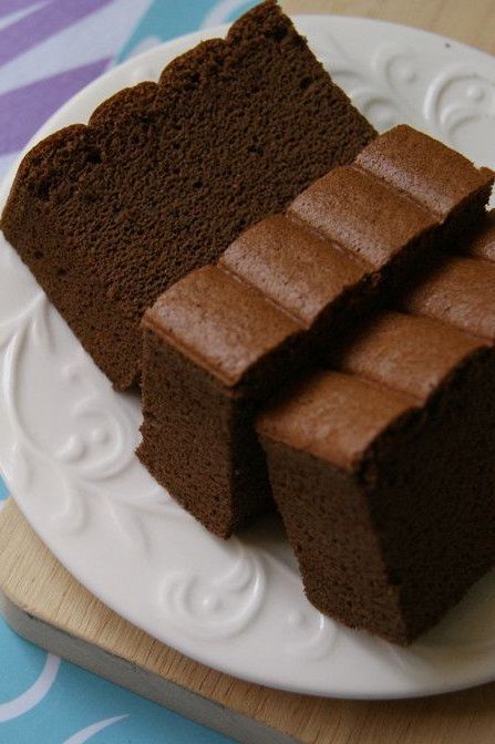 three pieces of chocolate cake on a plate with a wooden cutting board in the background