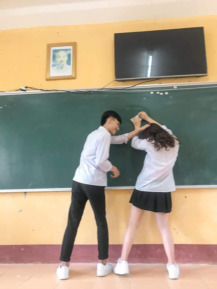 two people standing in front of a chalkboard with their hands on each other's head