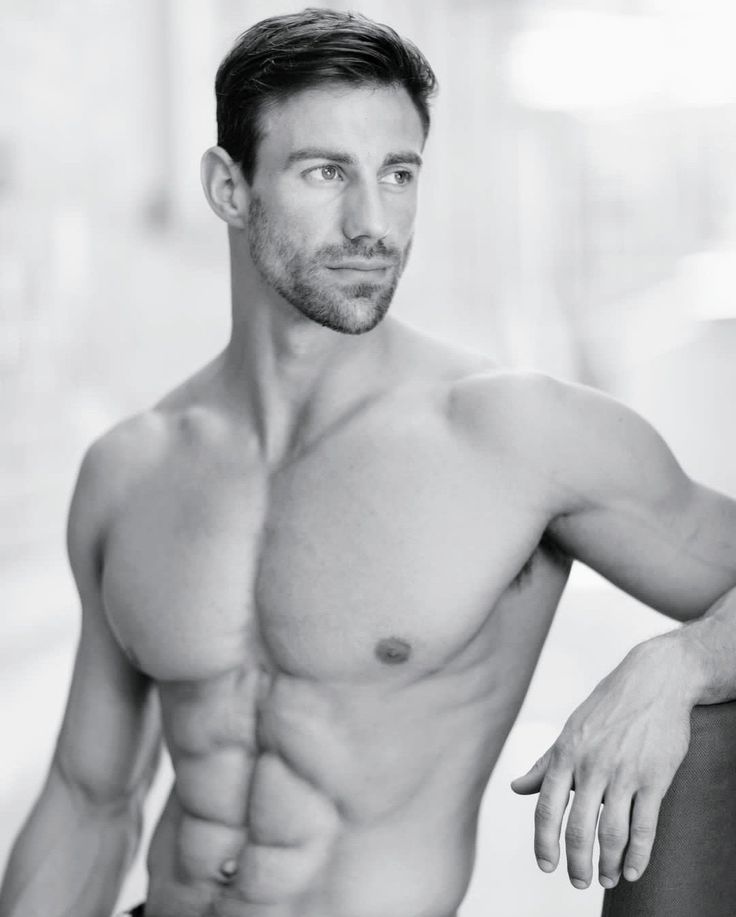 a shirtless man leaning against a wall with his hands on his hips and looking at the camera