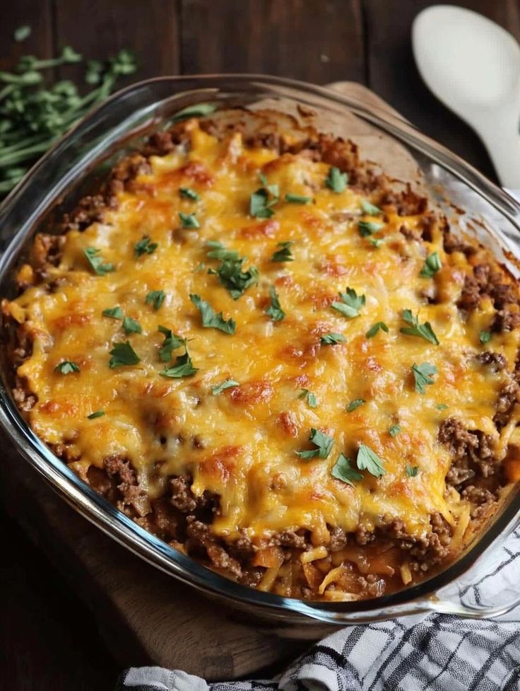 a casserole dish with meat and cheese in it on a wooden table next to utensils