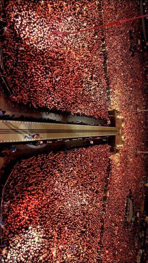 an aerial view of a crowd at a concert with lights on the ground and in the background