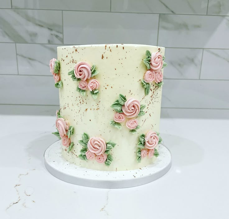 a white cake with pink roses on it sitting on a counter top next to a tile wall