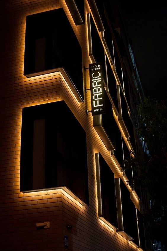 an illuminated sign on the side of a tall building at night with windows lit up