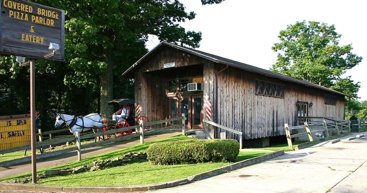 a horse drawn carriage parked in front of a wooden building with a sign on it's side