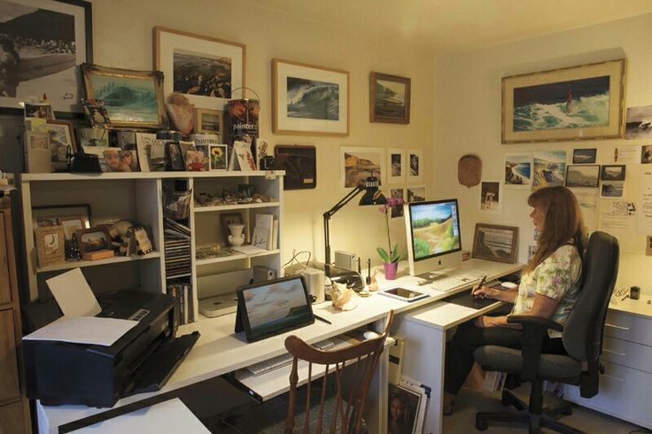 a woman sitting at a desk in front of a computer monitor and keyboard, with many pictures on the wall behind her