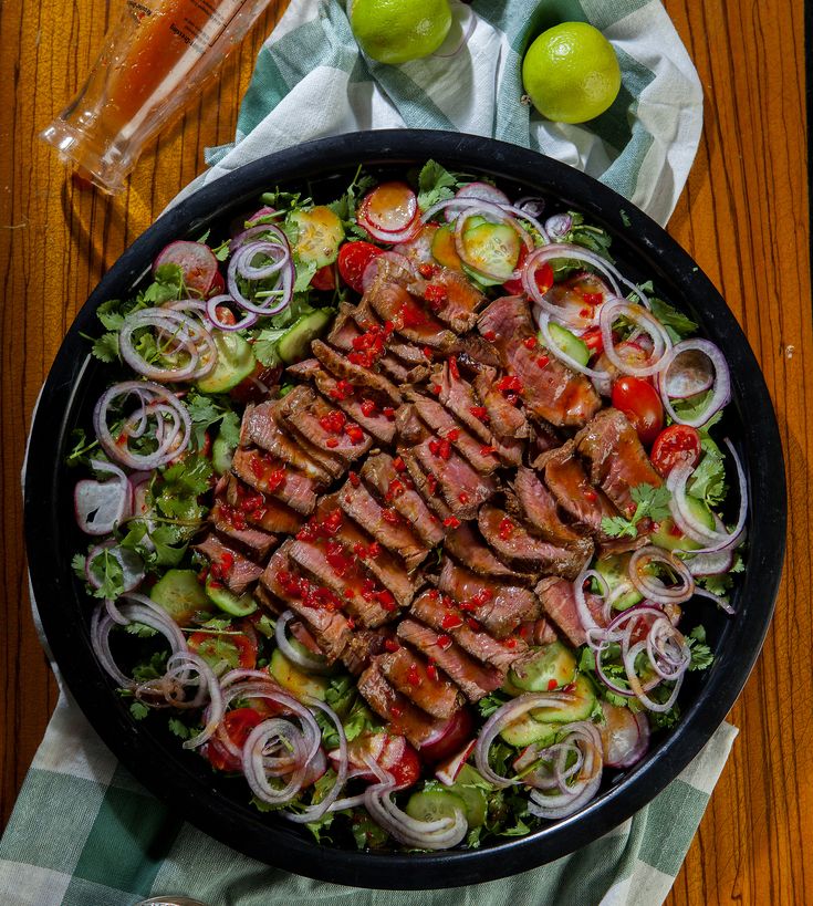 a plate with meat, onions and tomatoes on it next to a glass of water