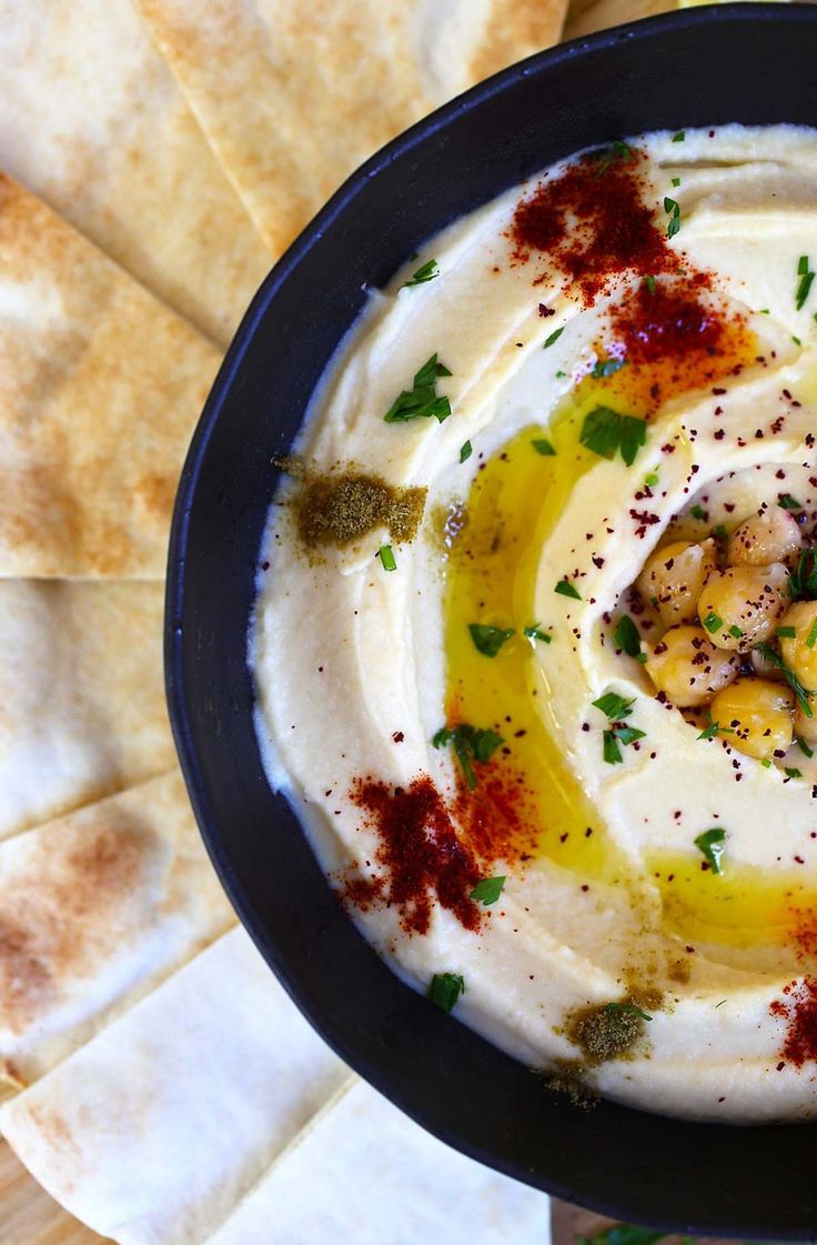 a black bowl filled with hummus and olives on top of pita bread