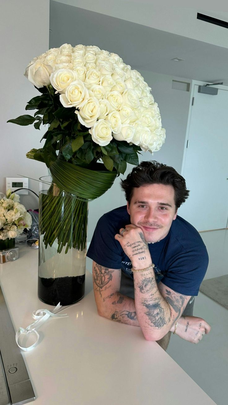 a man sitting at a table next to a vase with white roses