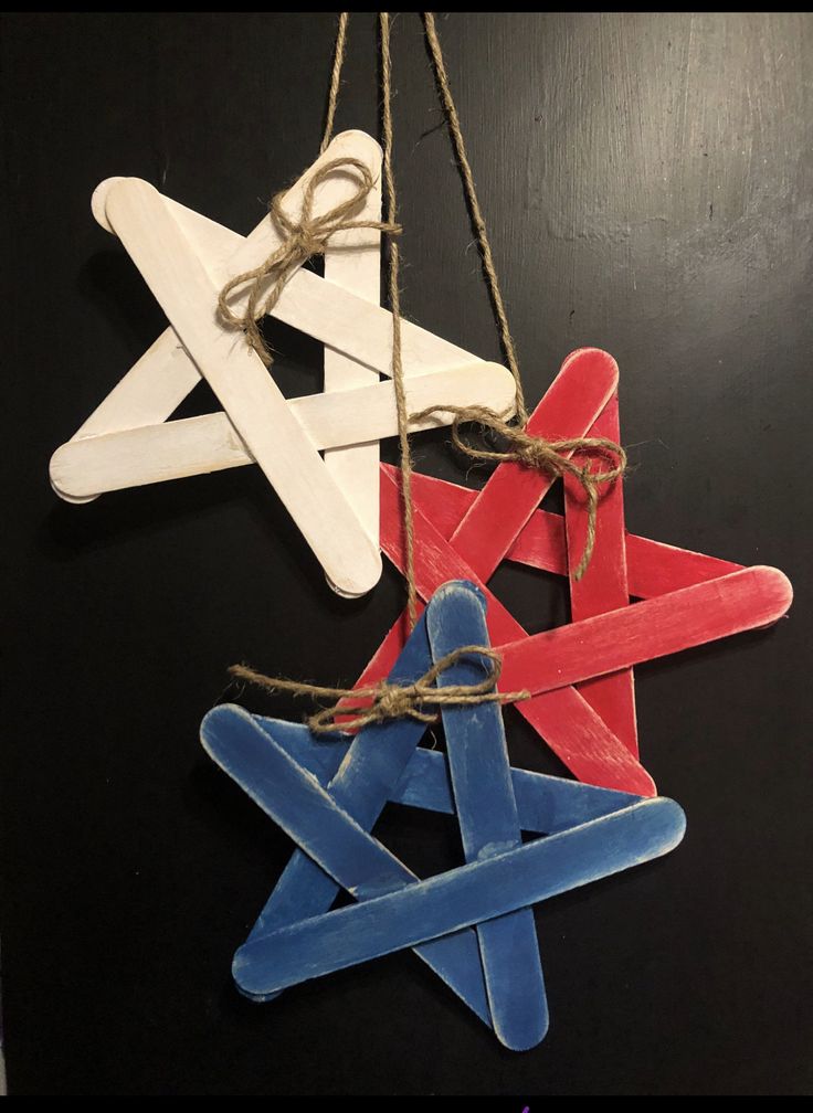 three popsicle star ornament hanging from twine on black table with string