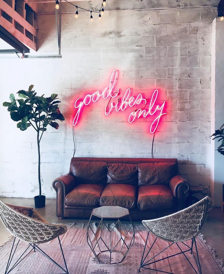 a living room with two chairs and a couch in front of a neon sign that says good quality