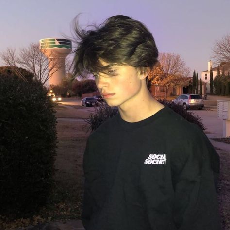 a young man wearing a black shirt standing in front of a parking lot