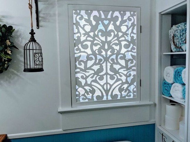 a white toilet sitting in a bathroom next to a window with decorative designs on it