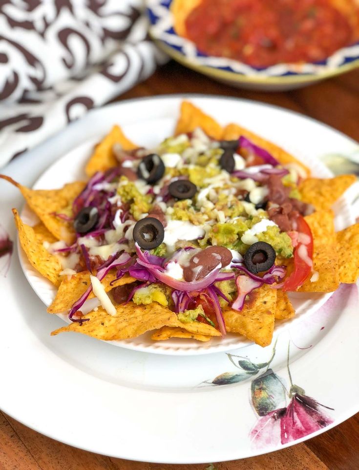 a white plate topped with nachos on top of a wooden table next to a bowl of salsa