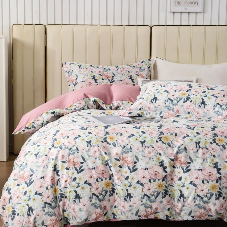 a bed with pink and white flowers on the comforter is in front of a radiator