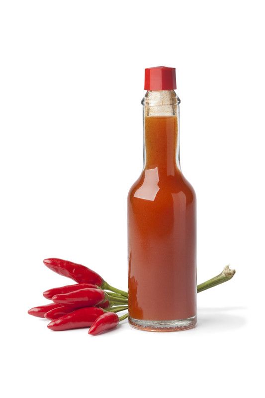 hot sauce in a glass bottle next to some red chili peppers on a white background