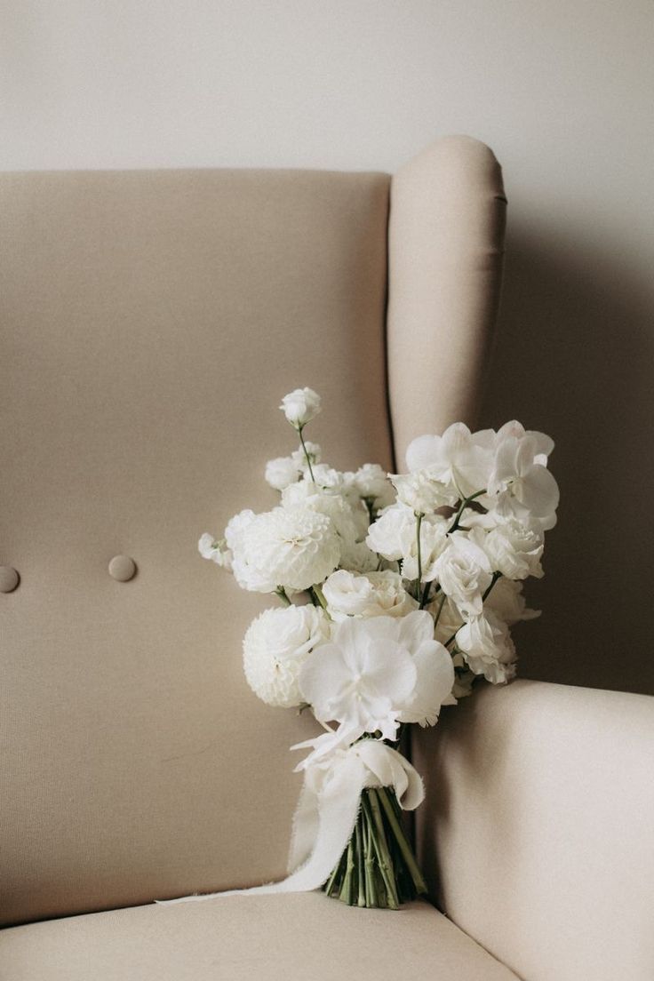 a bouquet of white flowers sitting on top of a beige chair next to a pillow