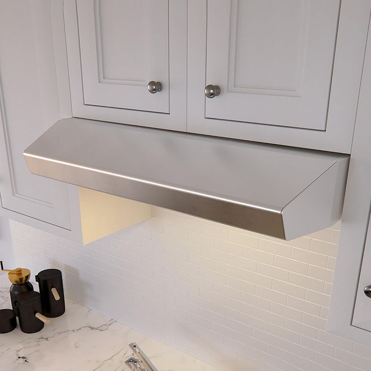 a stainless steel range hood in a white kitchen with marble counter tops and black accessories