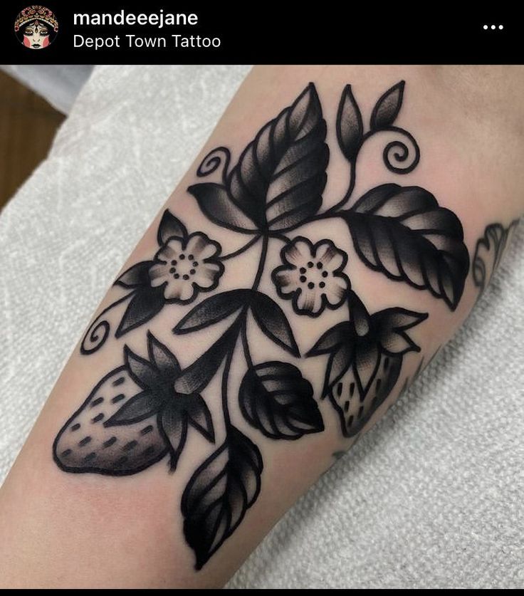 a black and white flower tattoo on the left arm, with leaves and flowers around it