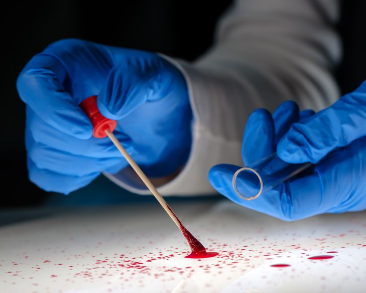 a person in blue gloves is holding a needle with blood on the table next to them