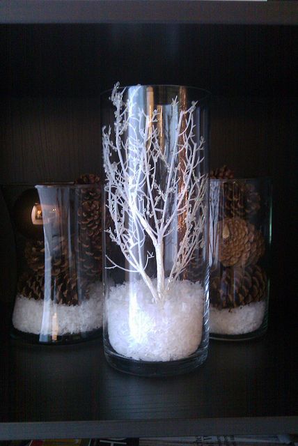 three glass vases with trees in them on top of a table next to pine cones