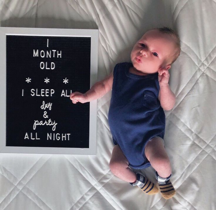 a baby laying on top of a bed next to a chalkboard that says i month old