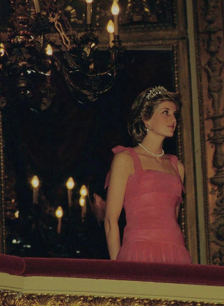 a woman in a pink dress standing next to a chandelier