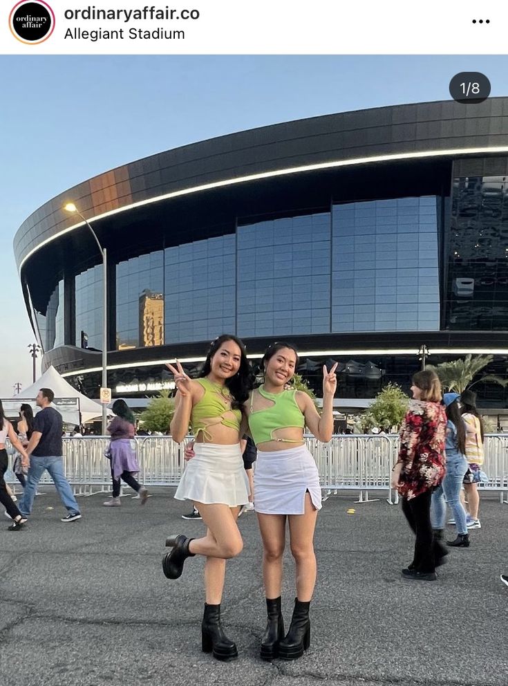 two young women standing in front of a large building with their hands up and smiling