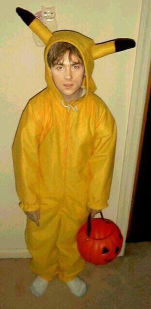 a young boy in a yellow costume holding a red pumpkin and wearing a devil mask