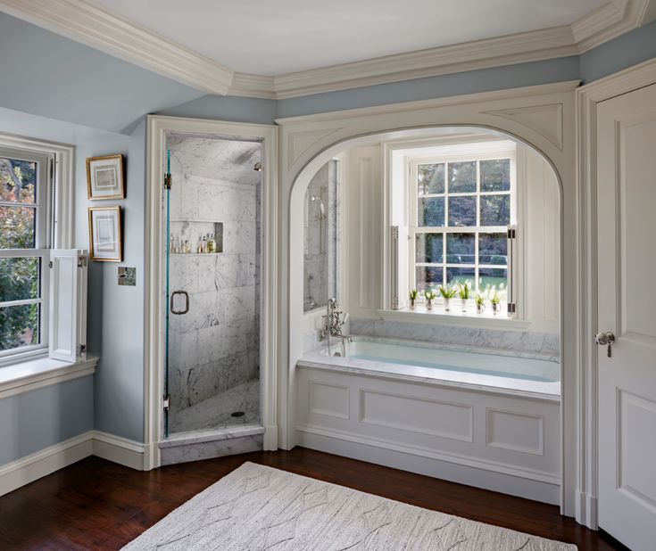 a bathroom with an arched window, tub and shower in the corner between two windows