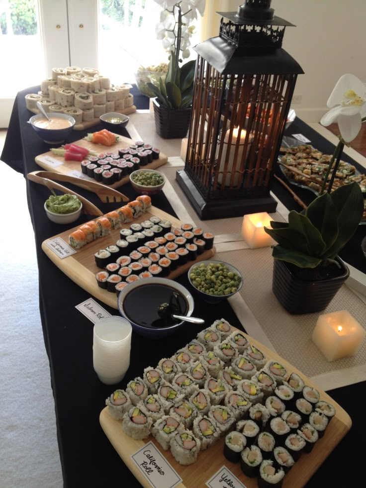 an assortment of sushi and other food items on a long table with candles in the background