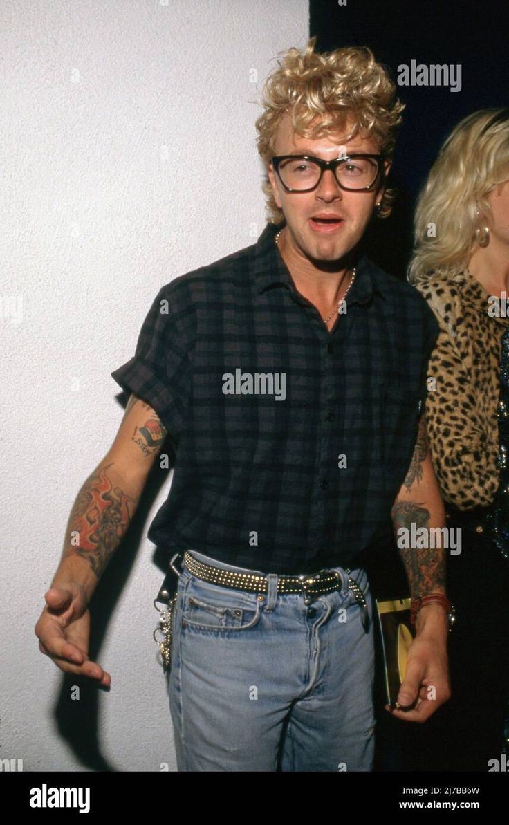 a man in glasses standing next to a woman with tattoos on his arms - stock image