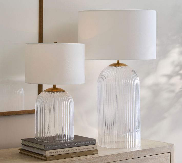 two clear glass lamps sitting on top of a wooden dresser next to a white lamp shade