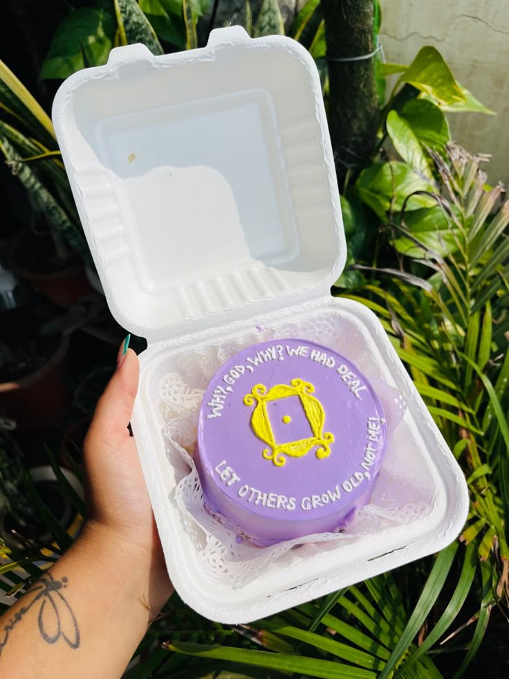 a person holding up a purple and white container with a yellow logo on the lid