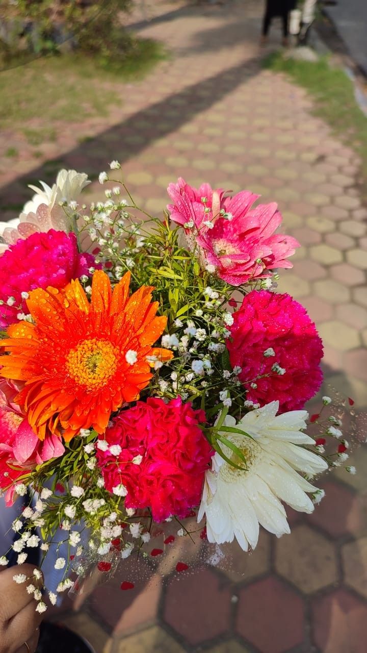 a person holding a bouquet of flowers in their hand on the sidewalk near a brick walkway