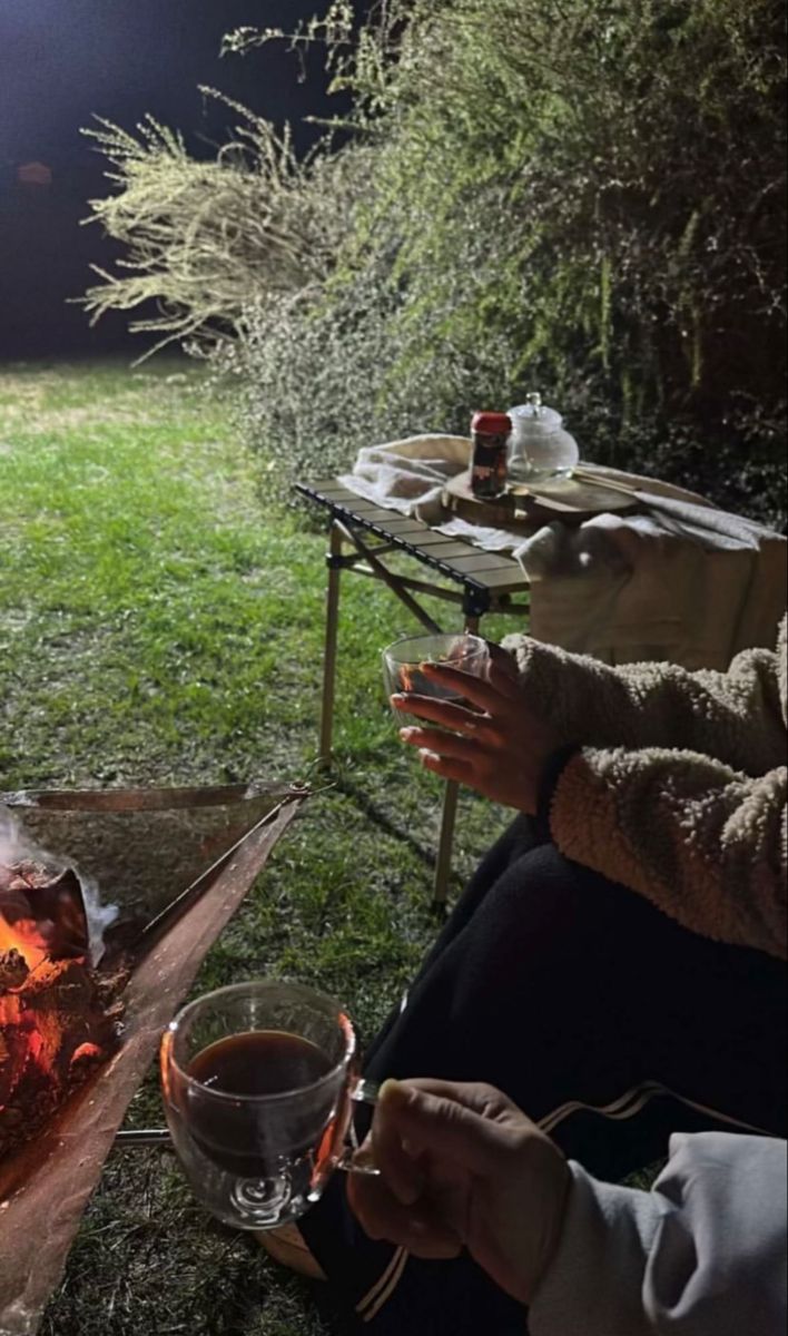 a person sitting in front of a campfire with a cup of coffee on it