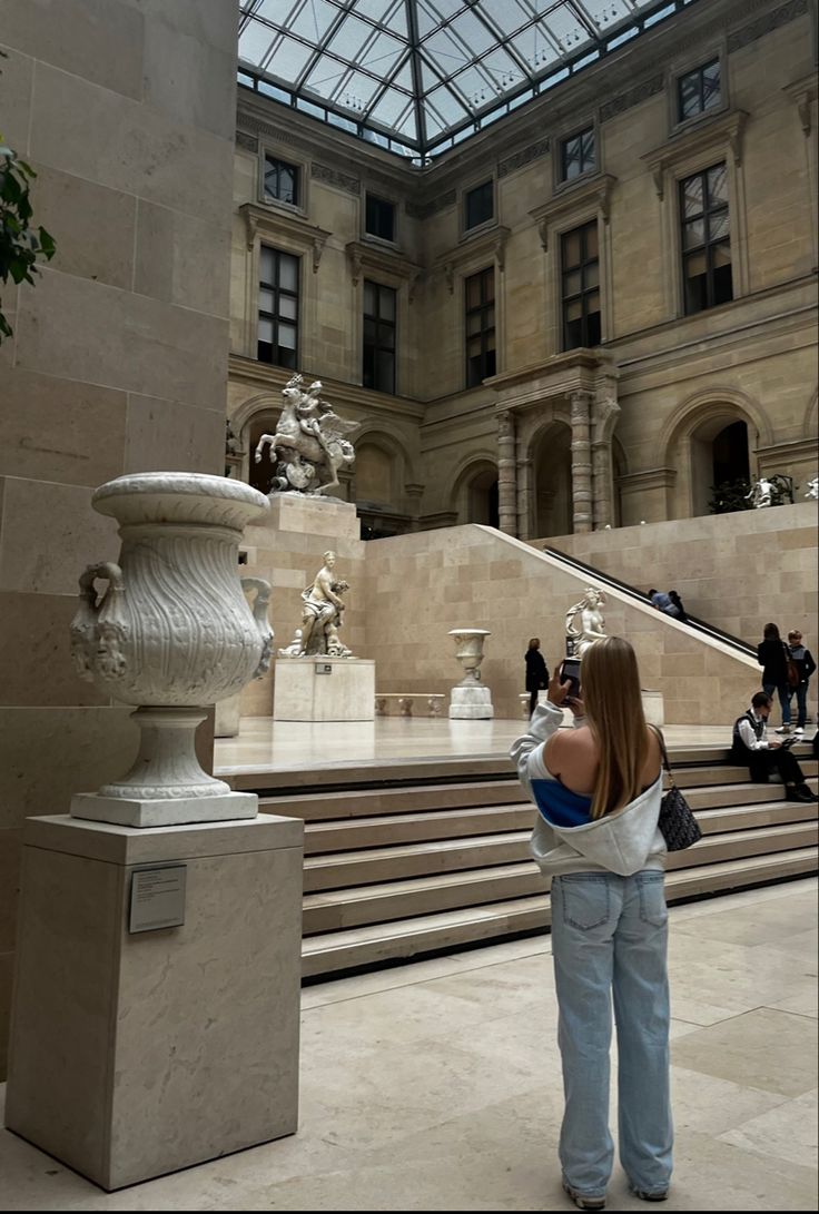 a woman is taking a photo in front of some stairs and statues at the metropolitan museum