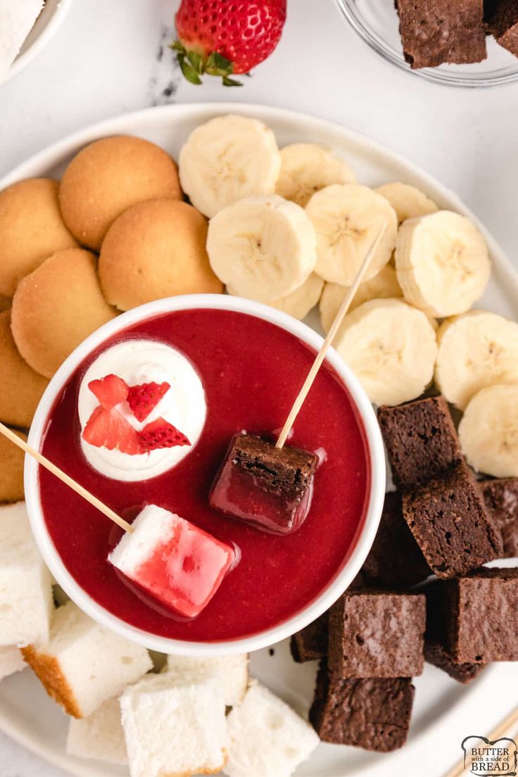 a white plate topped with desserts next to sliced bananas and strawberries on skewers